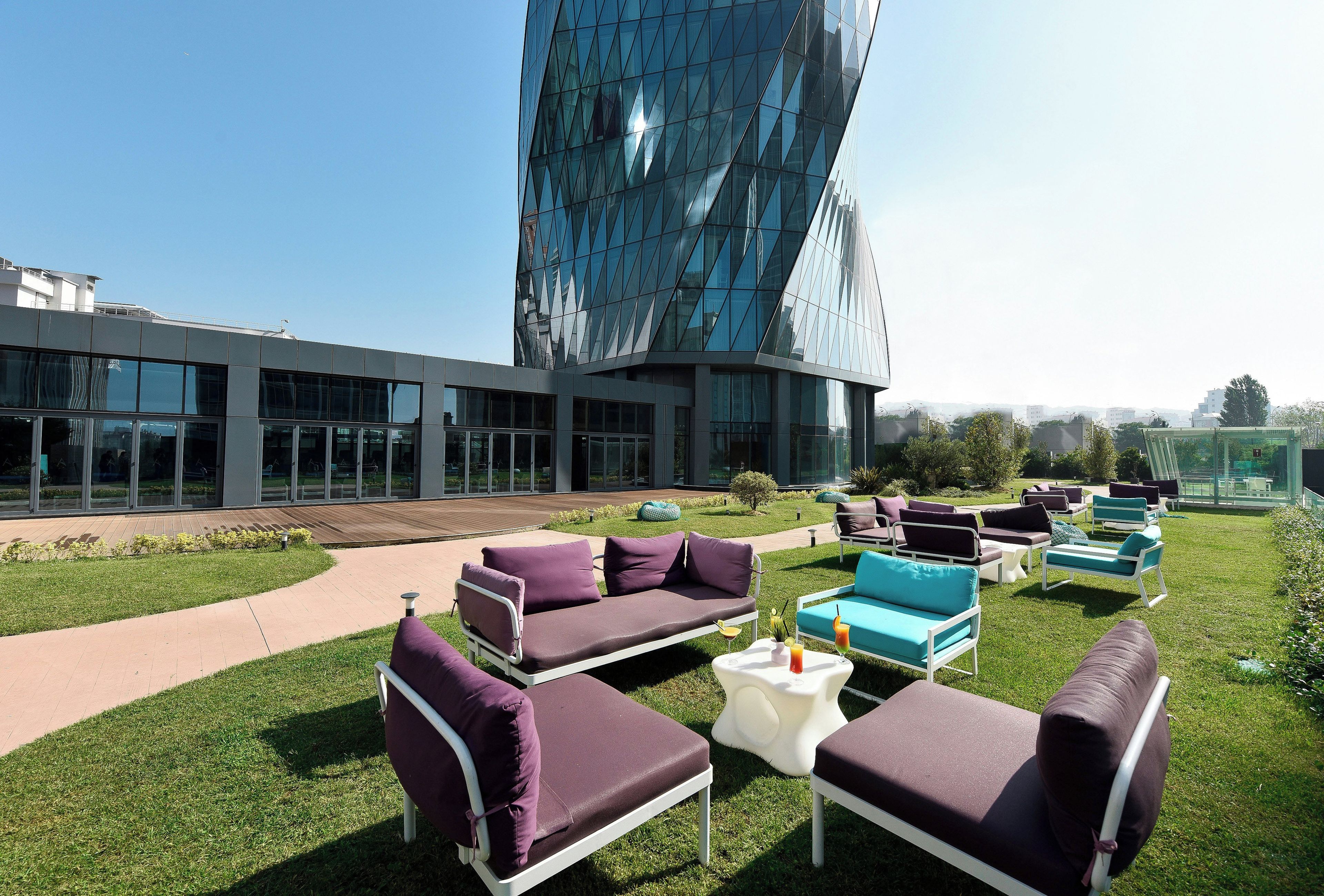 Un área de estar al aire libre con muebles modernos y un edificio de vidrio al fondo.