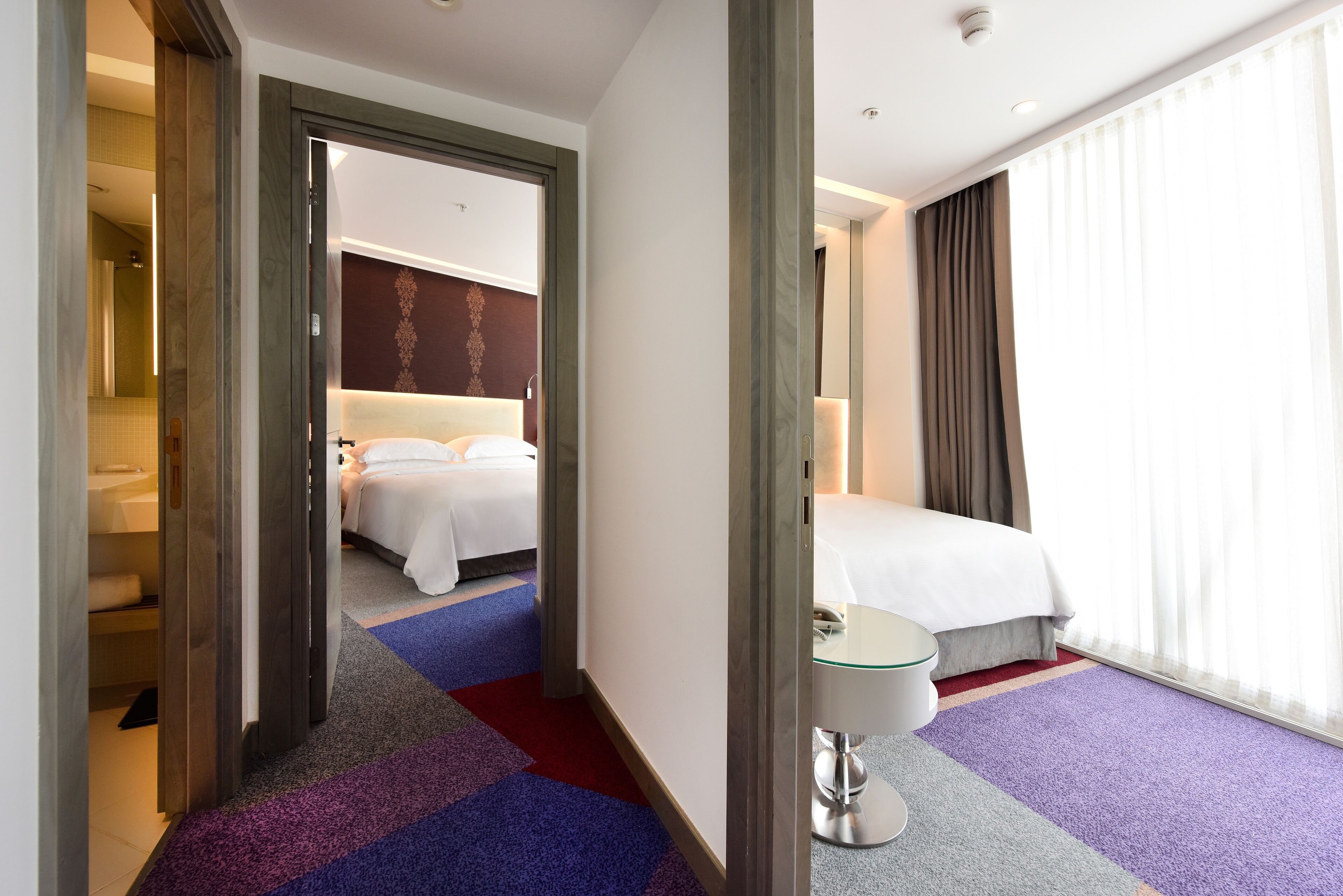 Una habitación de hotel con cama, mesita de noche y ventana con cortinas.