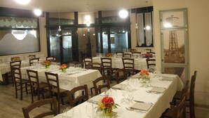 Un espace repas avec plusieurs tables dressées pour les convives, chacune étant agrémentée de chaises et de couverts.
