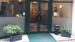 L’entrée d’un hôtel, avec un double portail, un paillasson vert et des plantes en pot.