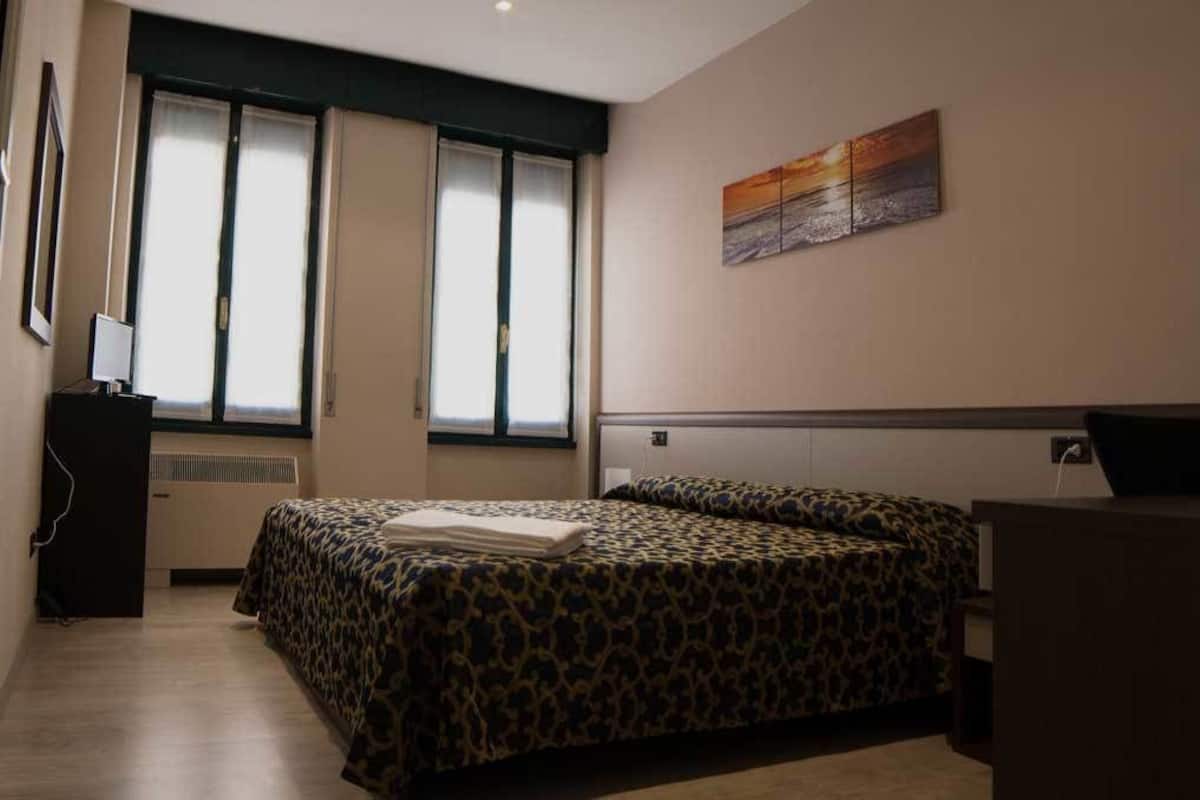 Une chambre d’hôtel avec un lit, un bureau et une fenêtre avec des rideaux.