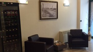 Un salon avec deux canapés noirs, une petite table, un réfrigérateur à vin et un tableau encadré au mur.