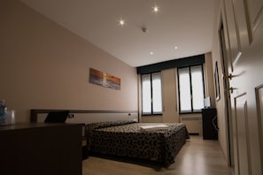 A bedroom with a bed, a desk, a window, and a painting on the wall.