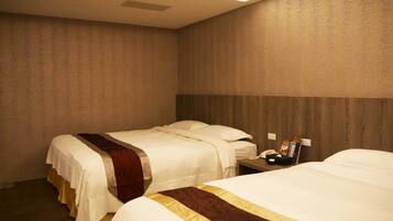 A hotel room with two beds, a wooden headboard, a bedside table with a phone and a magazine, and a wall-mounted light fixture.