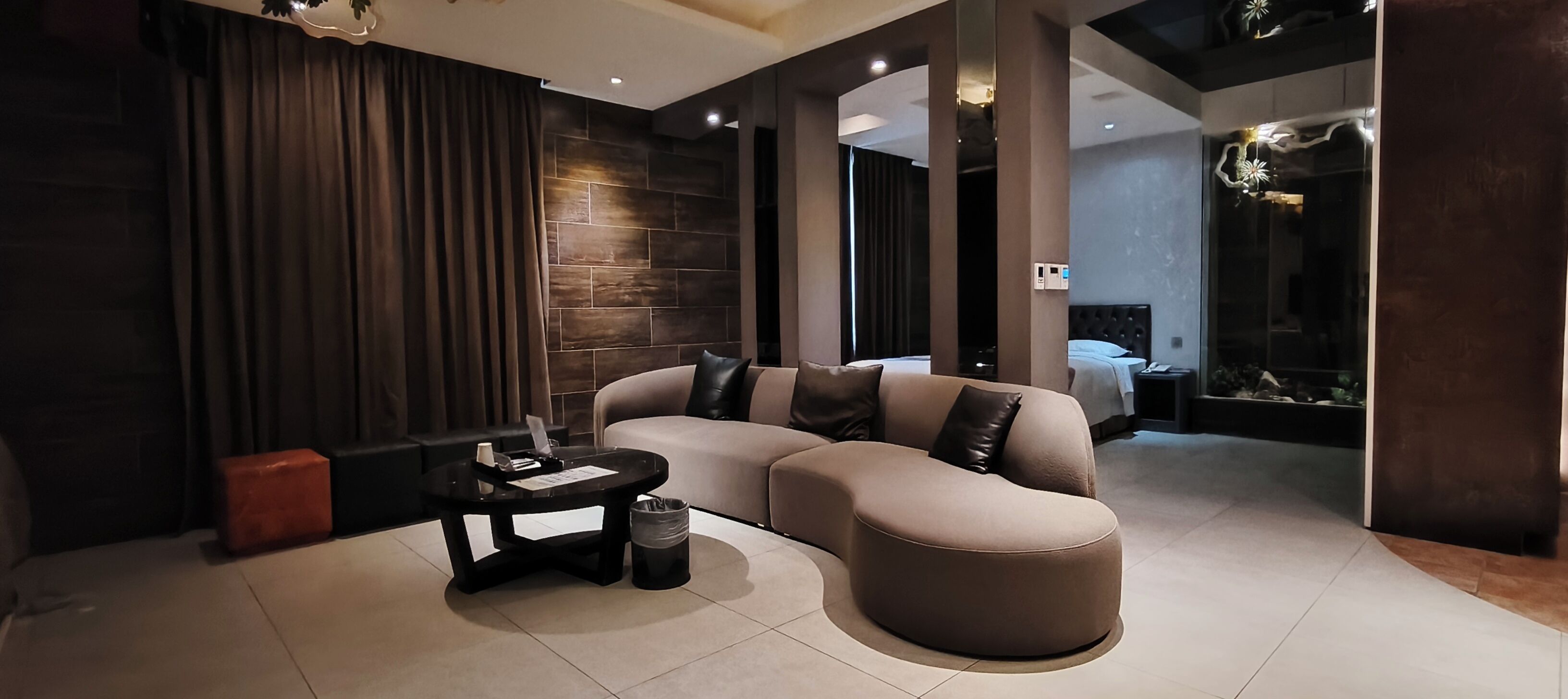 A modern hotel room with a curved sofa, a small side table, and a bed with a headboard.