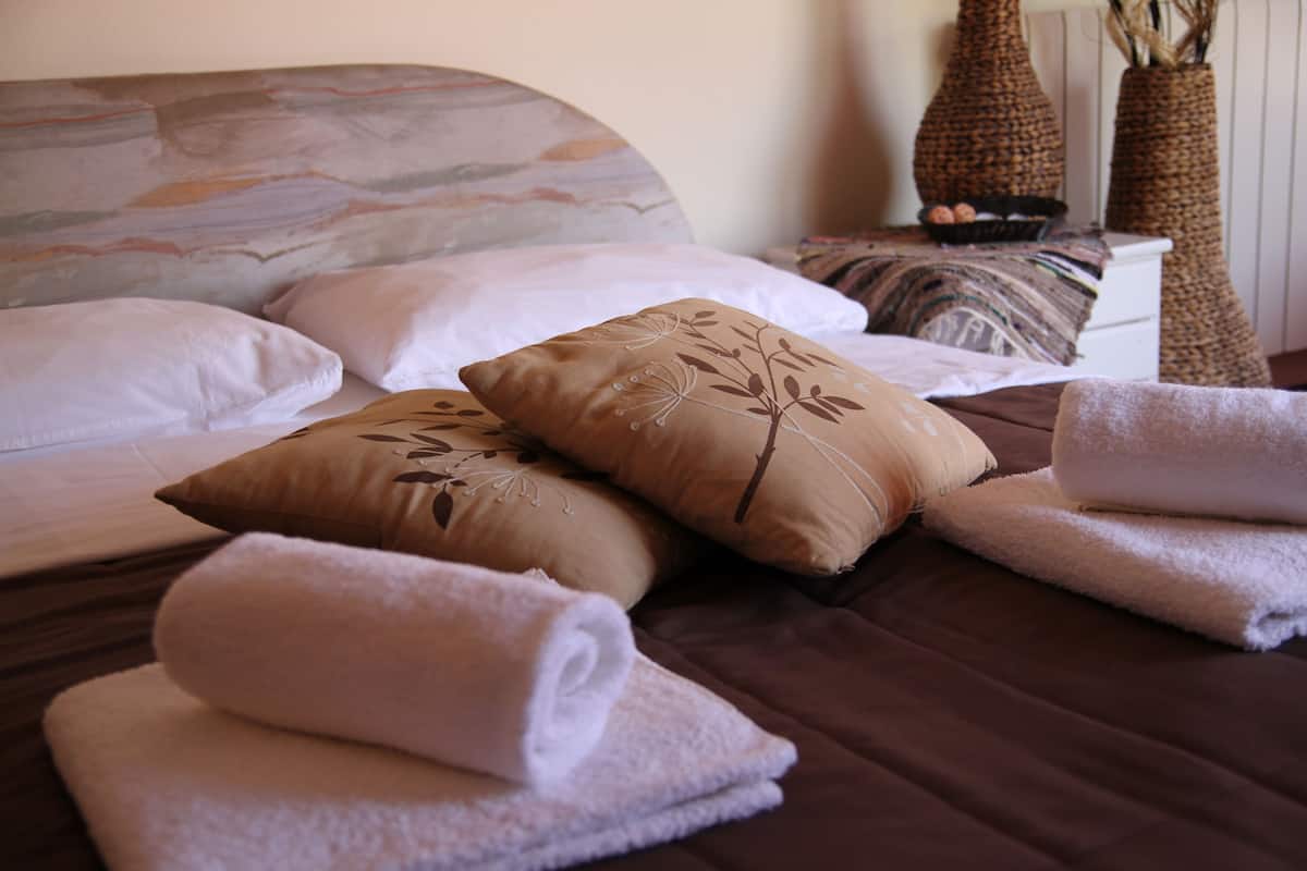 A neatly made bed with a brown headboard, multiple pillows, and folded towels.