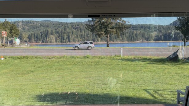 A view from a room with a large window overlooking a grassy area with a wooden deck and a road with a vehicle. - Foster Lake Inn (Sweet Home)