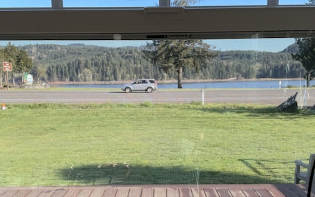 A view from a room with a large window overlooking a grassy area with a wooden deck and a road with a vehicle.
