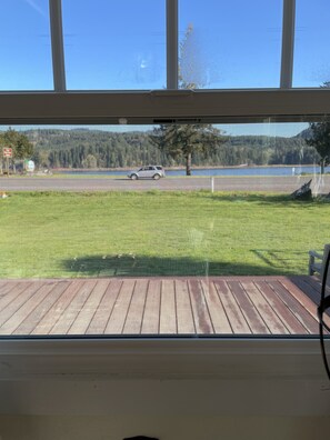 Vista desde una habitación con un ventanal grande que da a un área verde con una terraza de madera y una carretera con un vehículo.