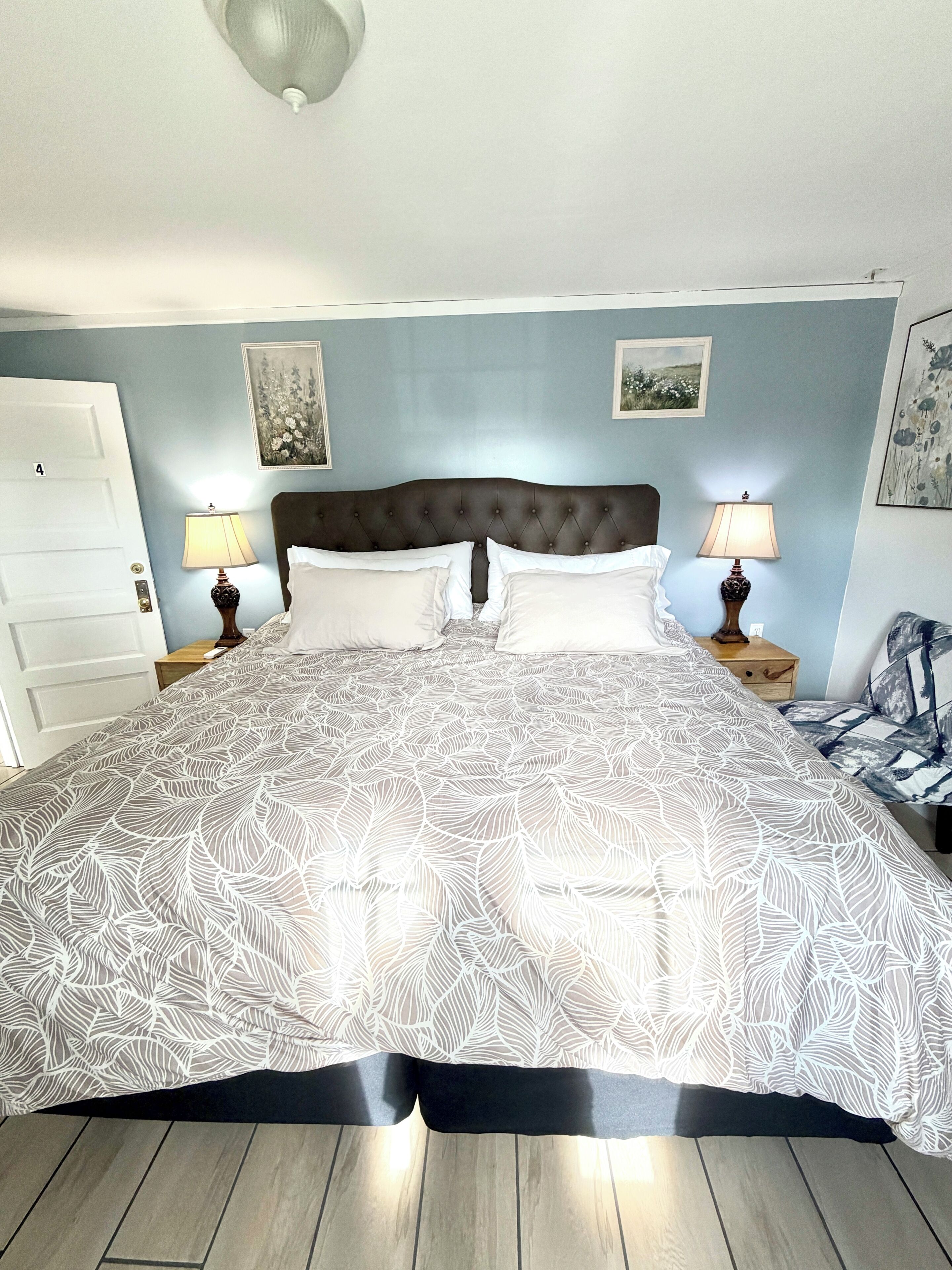 A bedroom with a large bed, two bedside tables with lamps, a door, and two framed pictures on the wall.