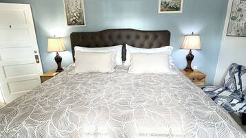 A bedroom with a large bed, two bedside tables with lamps, a door, and two framed pictures on the wall.