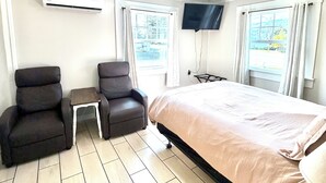 A hotel room with a bed, two armchairs, a small table, a TV, and an air conditioning unit. - Foster Lake Inn (Sweet Home)