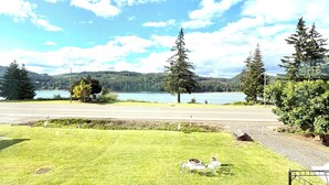 A grassy area with a bench, a small table, and chairs, a metal fence, and a view of a lake and trees in the distance. - Foster Lake Inn (Sweet Home)