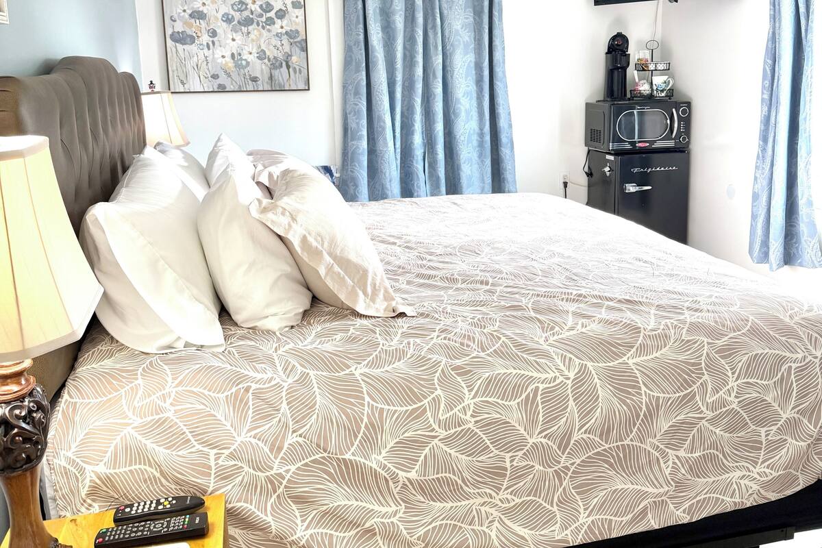 A neatly arranged bedroom with a bed, a bedside table with a lamp, a flat-screen TV, and a microwave.