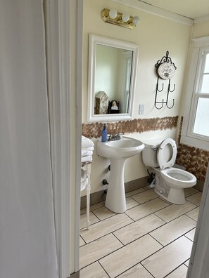 A bathroom with a sink, toilet, and mirror. There is a towel rack with towels and a decorative plate on the wall.