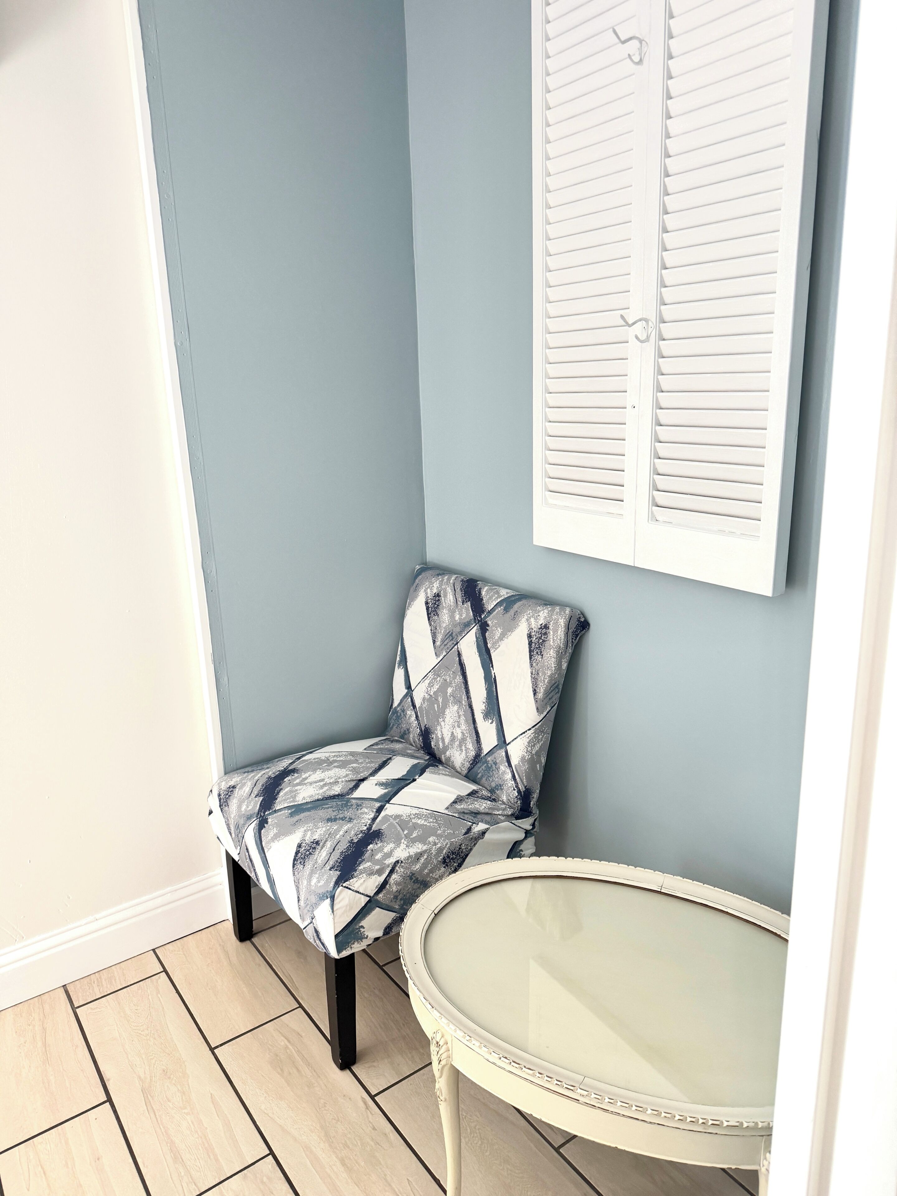 Una camera d'angolo con una parete blu, una sedia bianca con decorazioni blu e bianche e un tavolo bianco con piano in vetro.