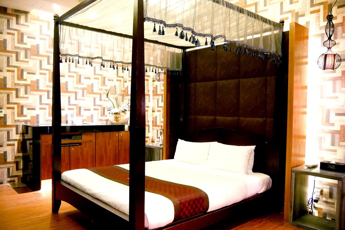 Una cama con dosel, un cabecero de madera y una mesita de noche con lámpara.