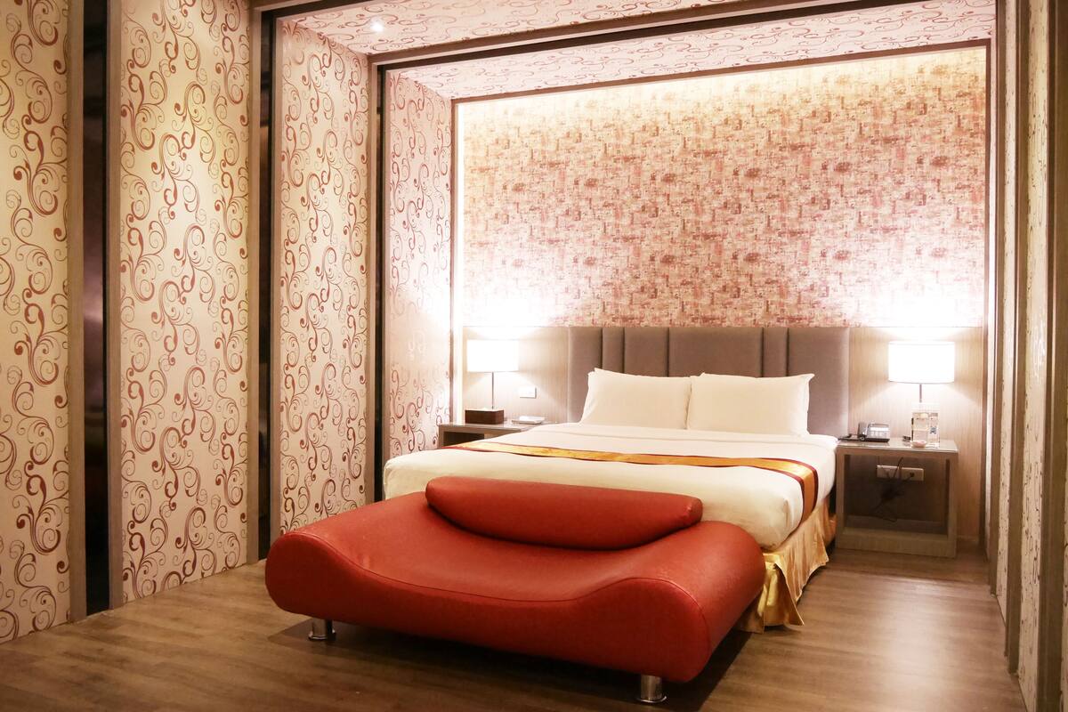 Una habitación de hotel moderna con una cama grande, un reposapiés rojo y papel tapiz estampado.