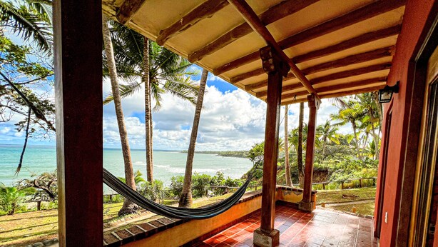 A covered porch with a hammock, palm trees, and a view of the ocean. - Hotel Punta Franca (Punta Mala)