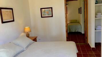 Un dormitorio con una cama, una mesita de noche con lámpara, un mapa en la pared y una puerta que da a otra habitación.