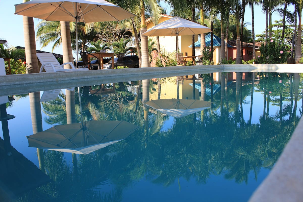 Piscina cristalina con reflejos de sombrillas y palmeras.