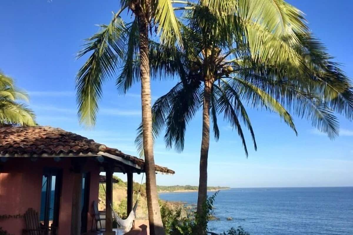 Una propiedad costera con una estructura de techo de paja, palmeras y vista al mar.