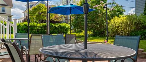 A patio with a round metal table and chairs, blue umbrellas, and a brick floor.