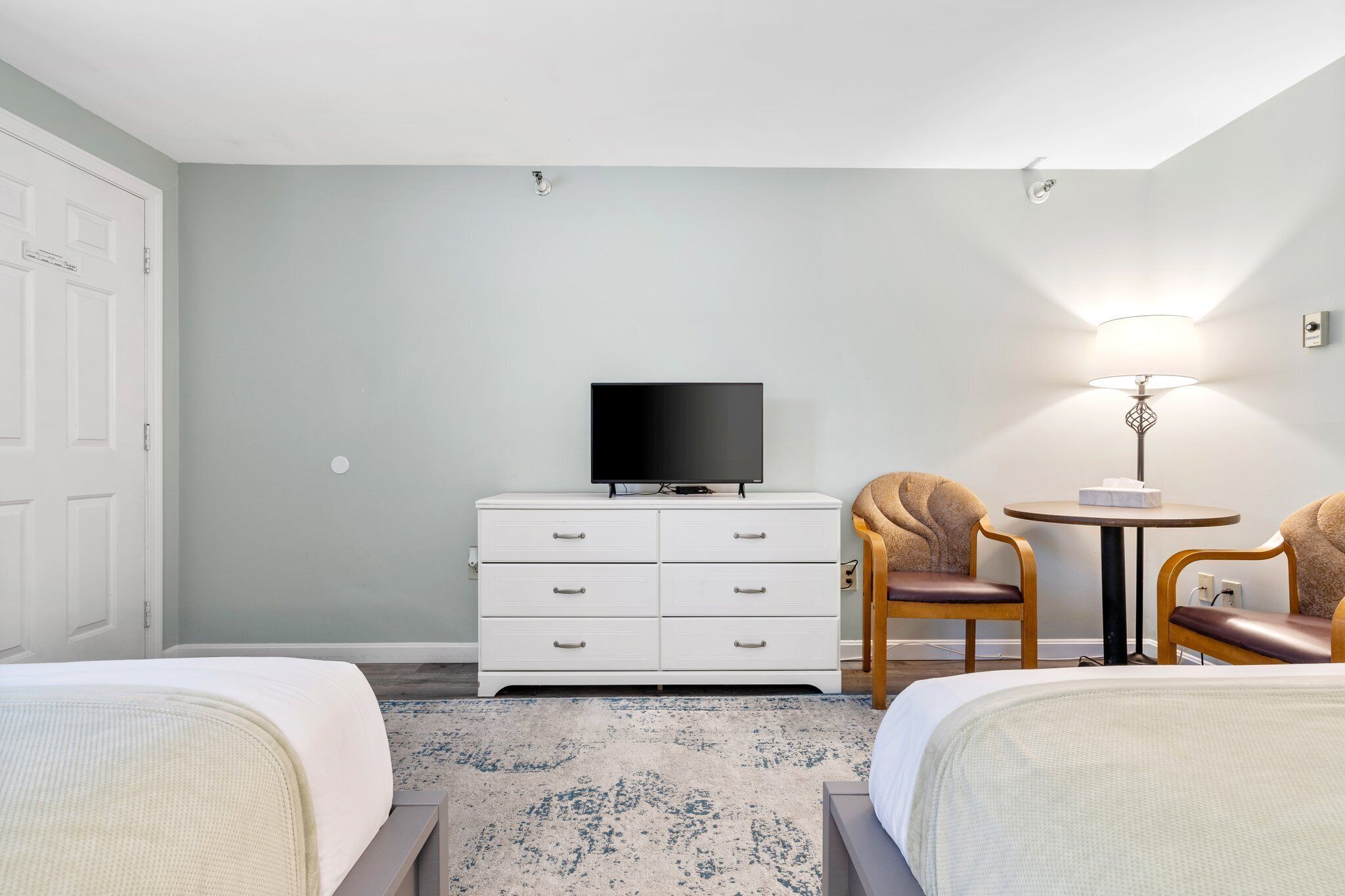 A hotel room with two beds, a TV on a dresser, a small table with chairs, and a lamp.
