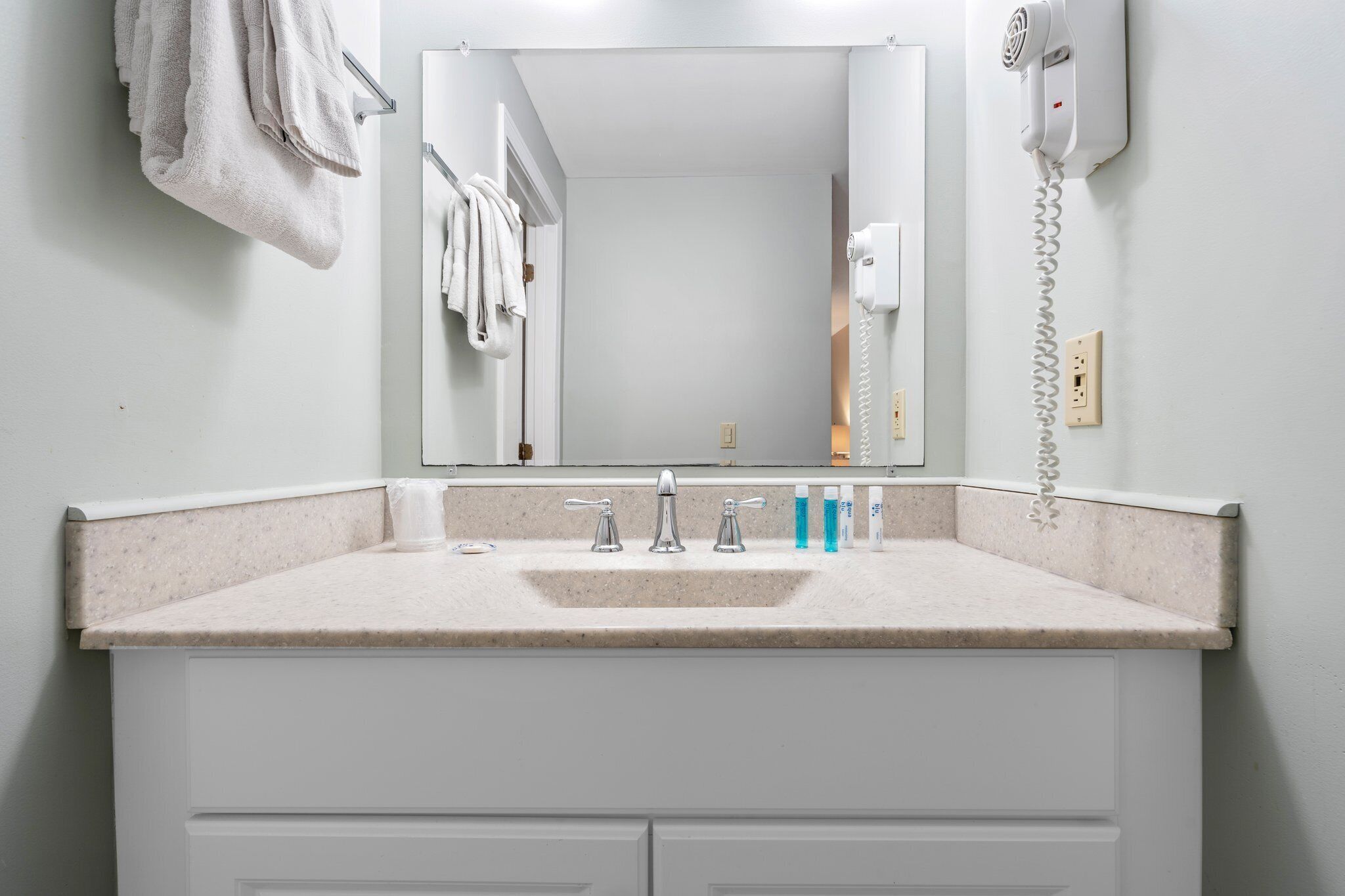 A bathroom with a sink, two faucets, a mirror, a hairdryer, and a telephone.