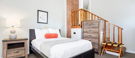 Un dormitorio con cama, mesita de noche, cómoda y una silla de madera.