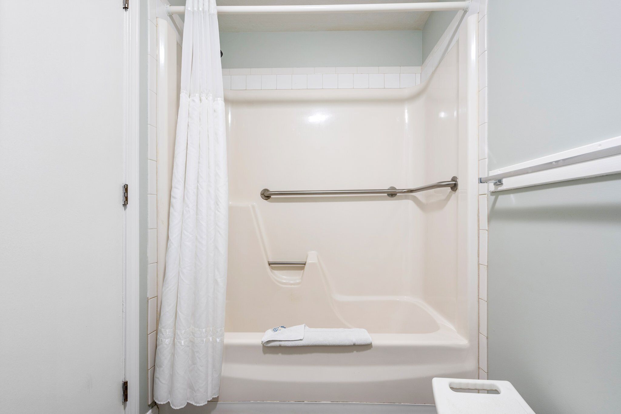 A white shower with a grab bar, a towel rack, and a white shower curtain.