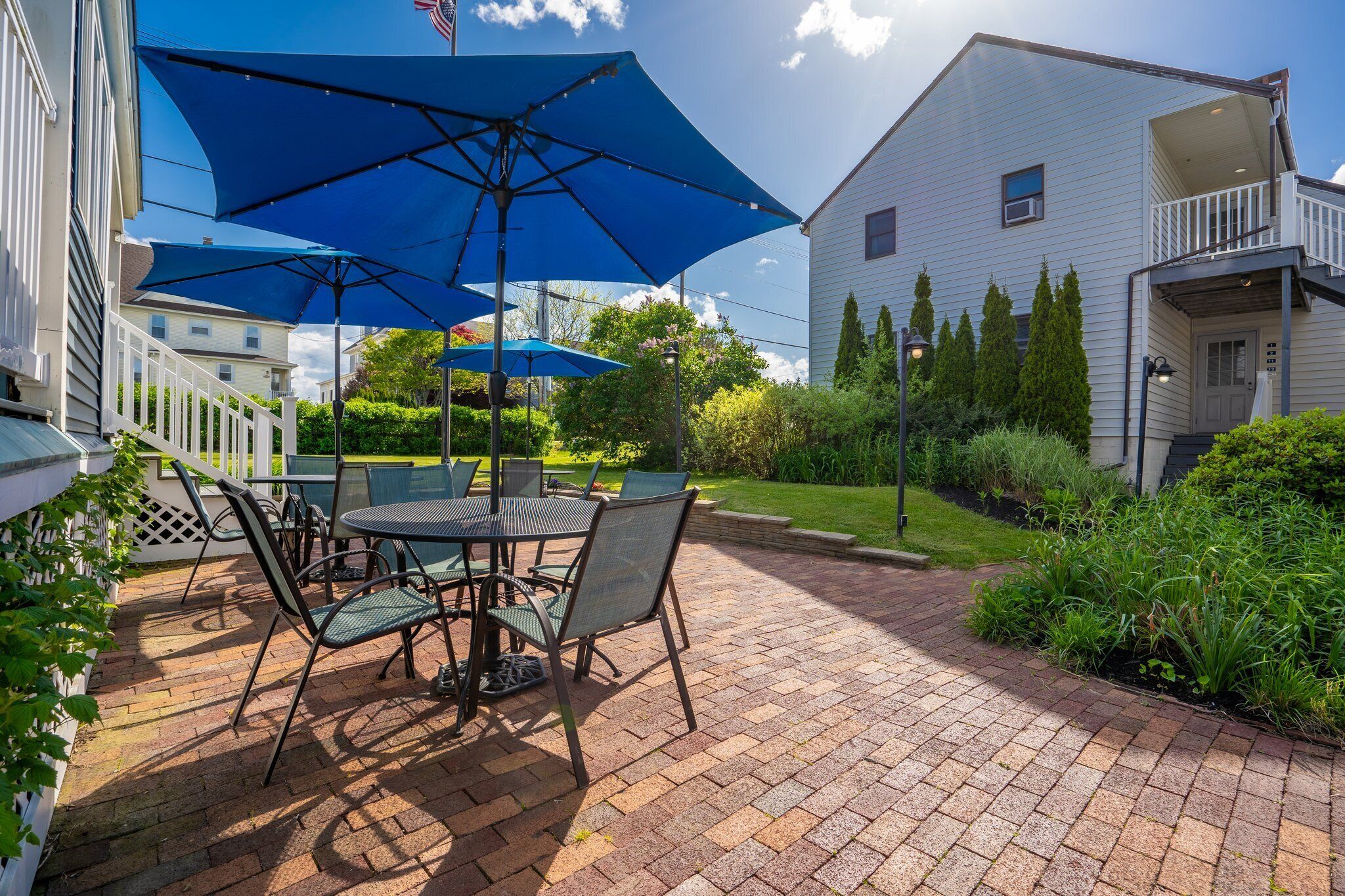 Une terrasse avec une table et des chaises, un grand parasol bleu et un bâtiment blanc en arrière-plan.