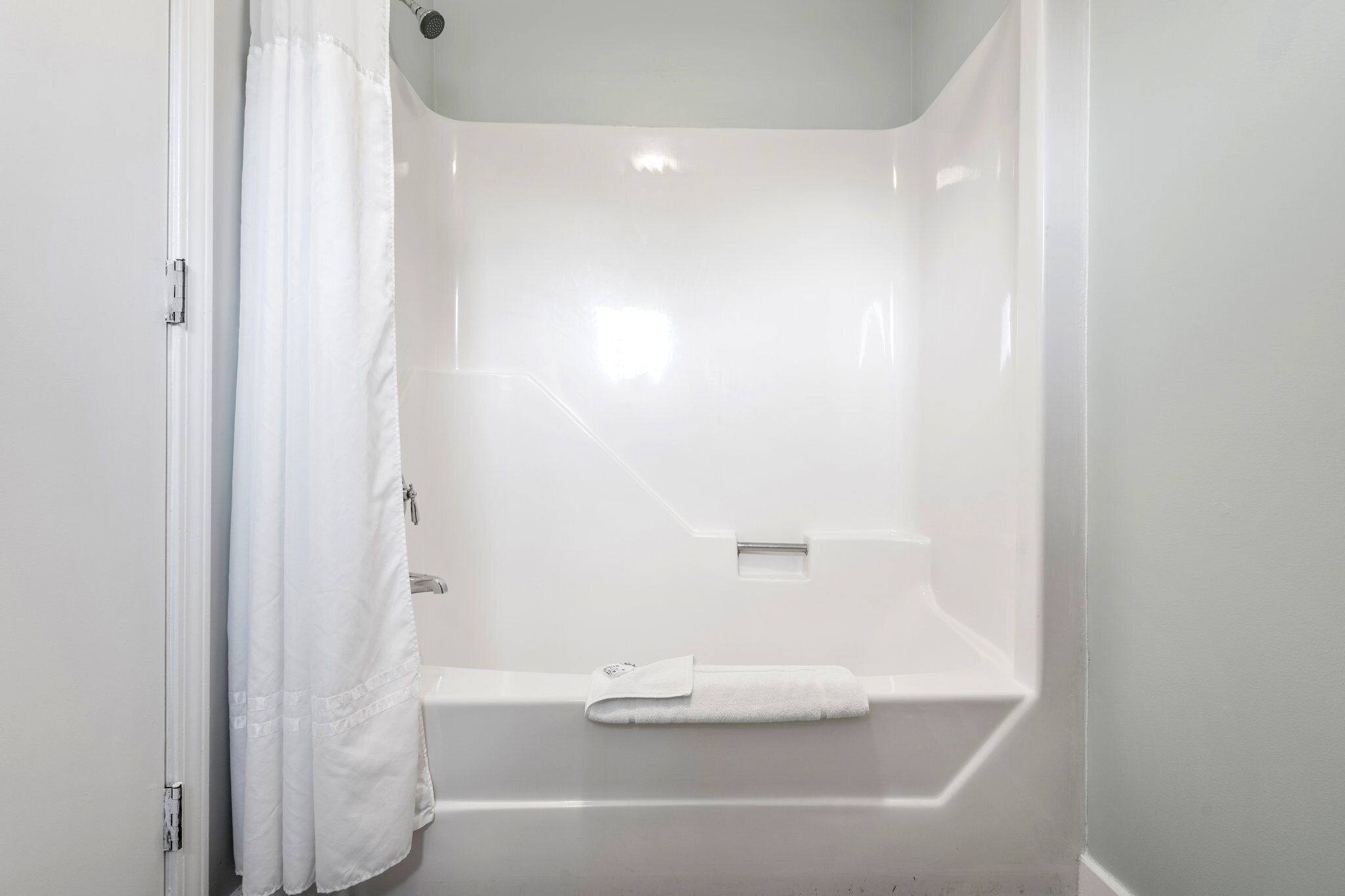 A white bathroom with a bathtub, a shower curtain, and a towel on the tub.