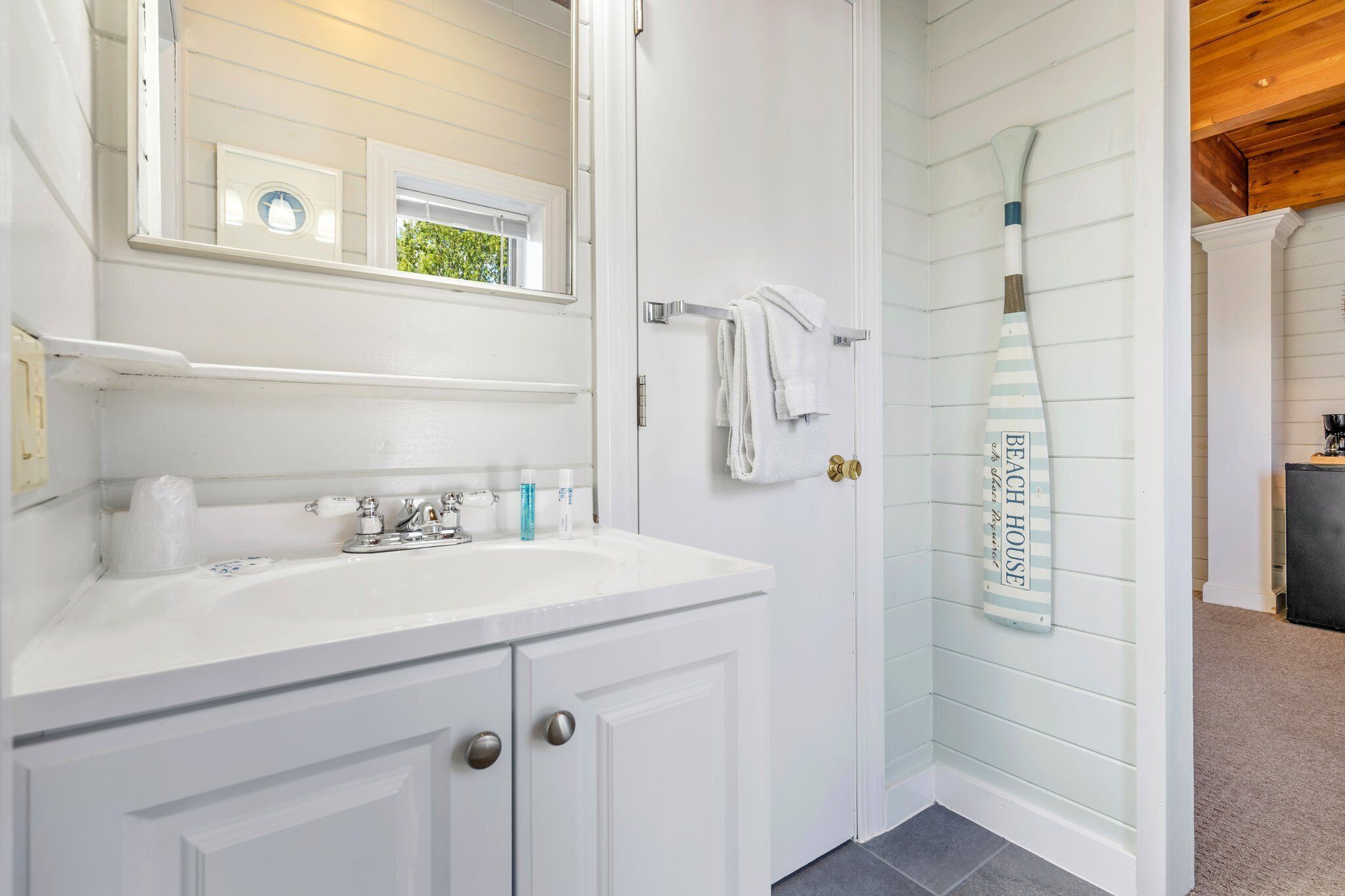 A bathroom with a white vanity, a mirror, a towel rack, and a shower with a towel hanging on the wall.
