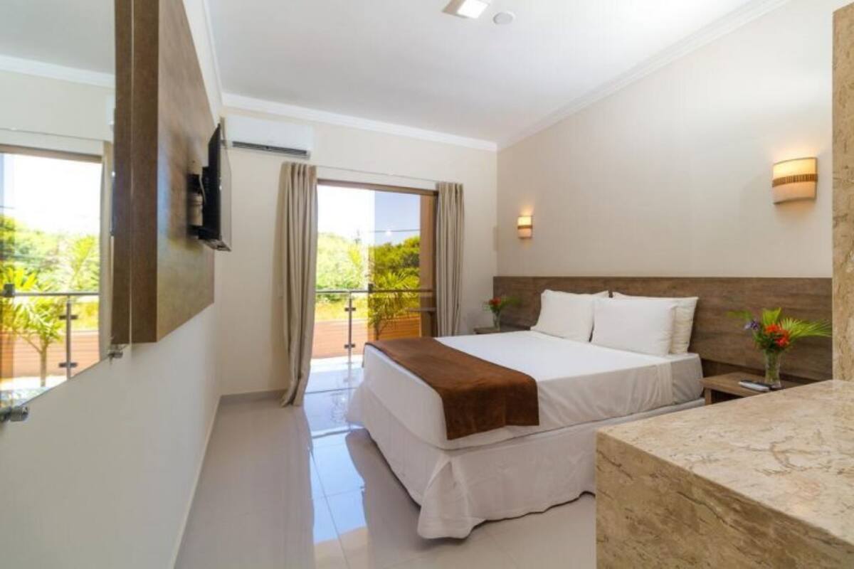 A modern hotel room with a large bed, a bathroom with a marble countertop, and a balcony with curtains.