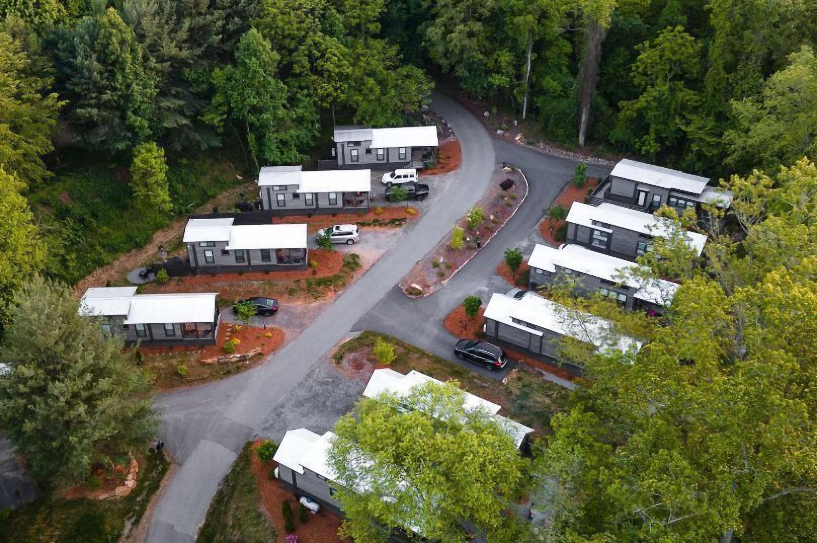 Vista aérea de um camping com várias cabanas, uma estrada sinuosa e floresta densa ao redor.