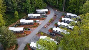 Vista aérea de um camping com várias cabanas, uma estrada sinuosa e floresta densa ao redor.