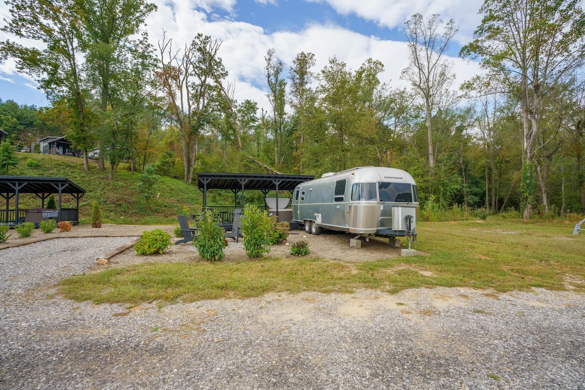 Un véhicule récréatif (VR) est stationné dans un terrain de camping, où se trouvent des tables de pique-nique et des espaces abrités.