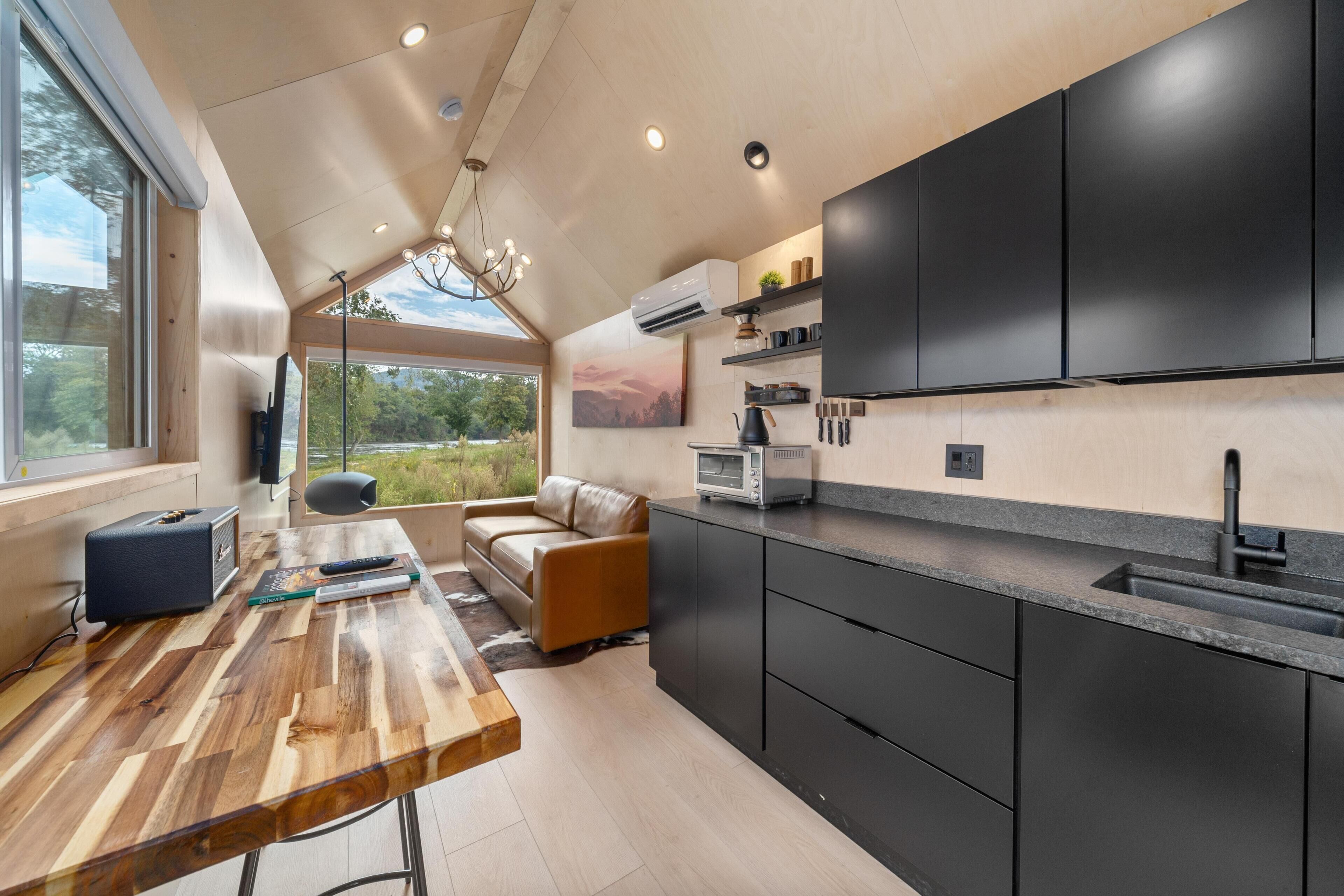 A modern kitchen with a wooden dining table, a sofa, and a view of the outdoors.
