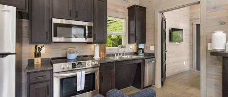 A modern kitchen with dark wood cabinets, stainless steel appliances, a built-in microwave, and a large window providing natural light.