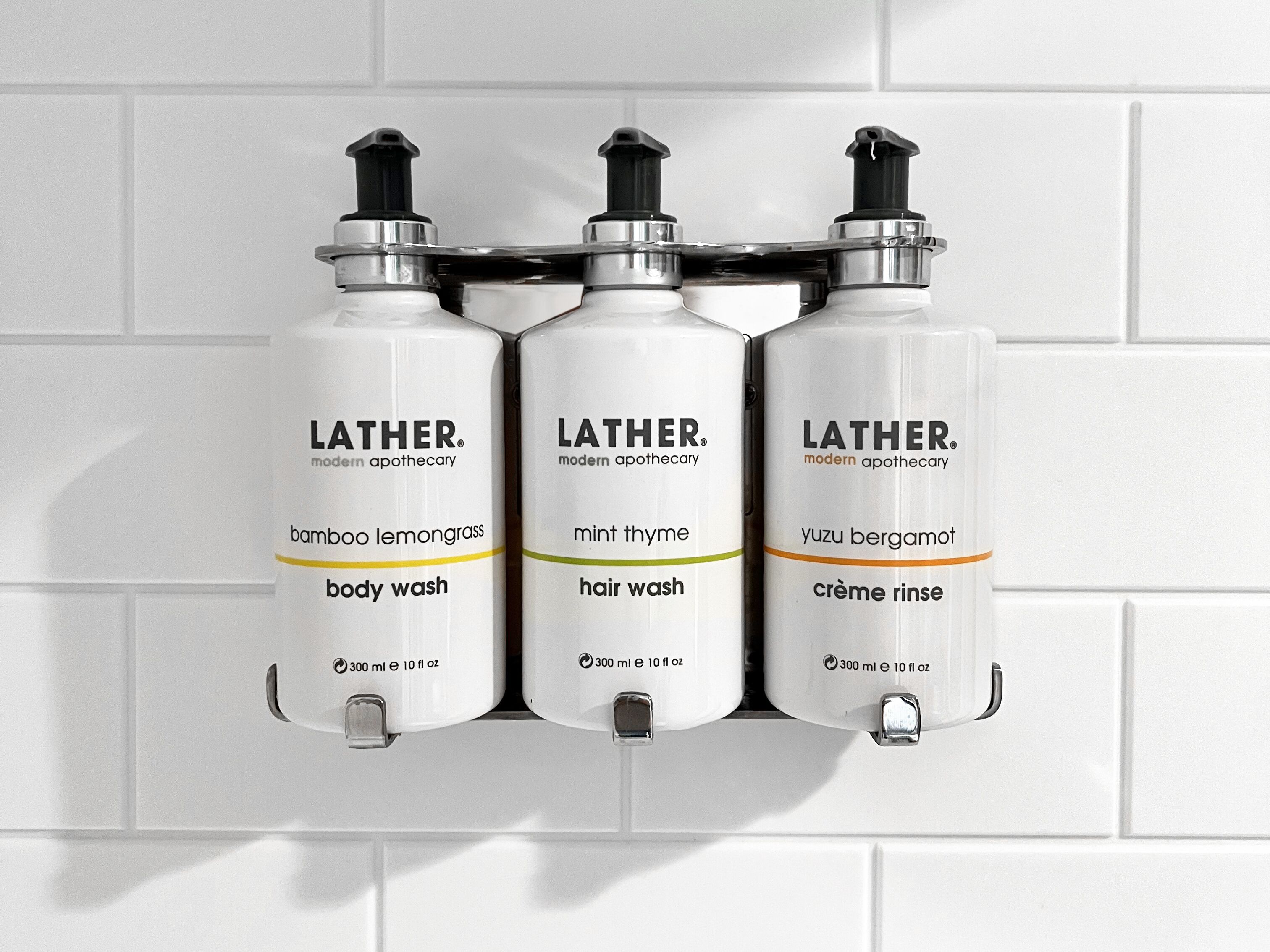 Drie flessen Lather douchegel op een witte betegelde muur.