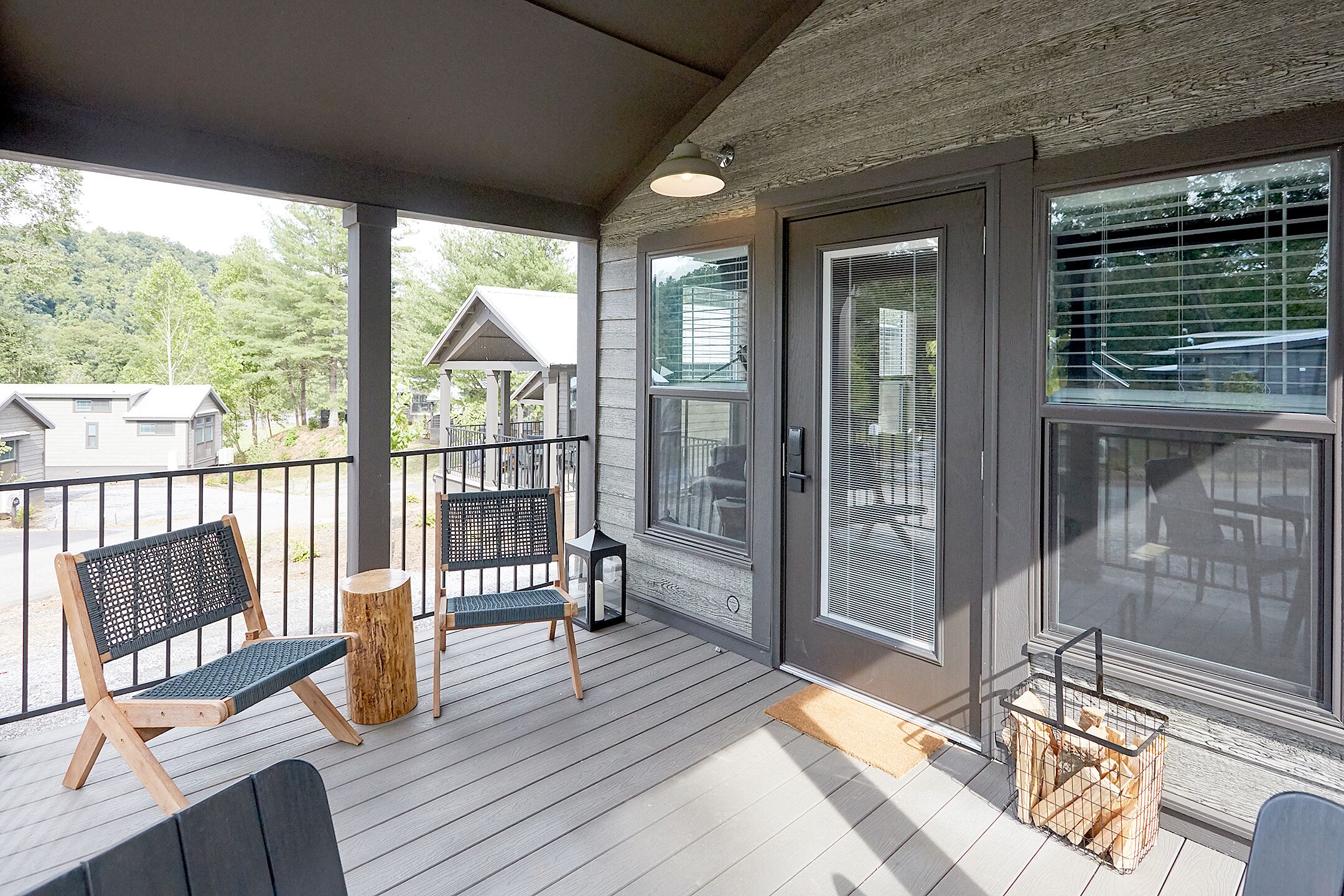 A covered porch with wooden flooring, two wooden chairs with mesh backs, a small wooden table, and a metal basket.