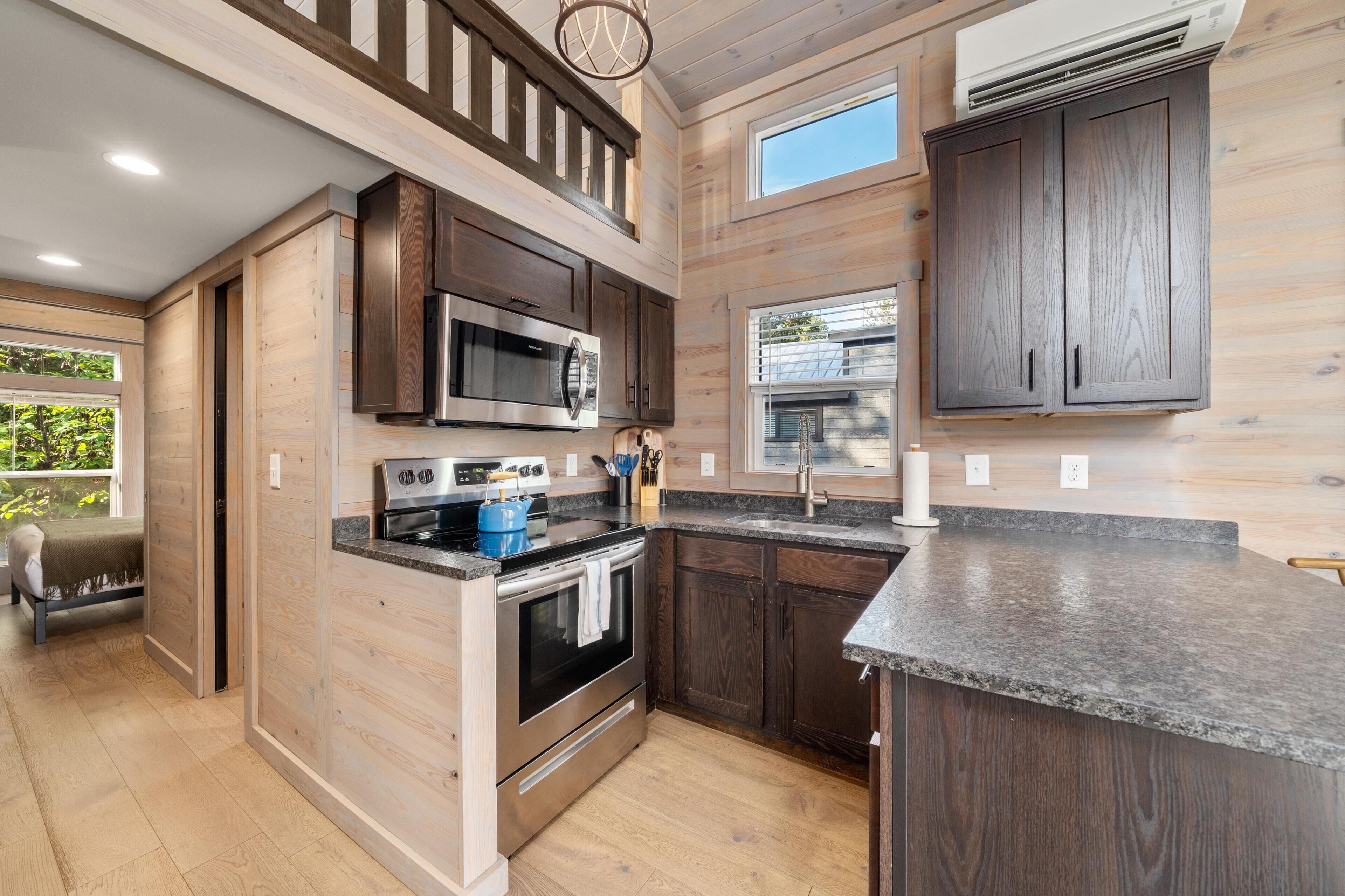 A kitchen with wooden cabinetry, a microwave, an oven, and a sink.