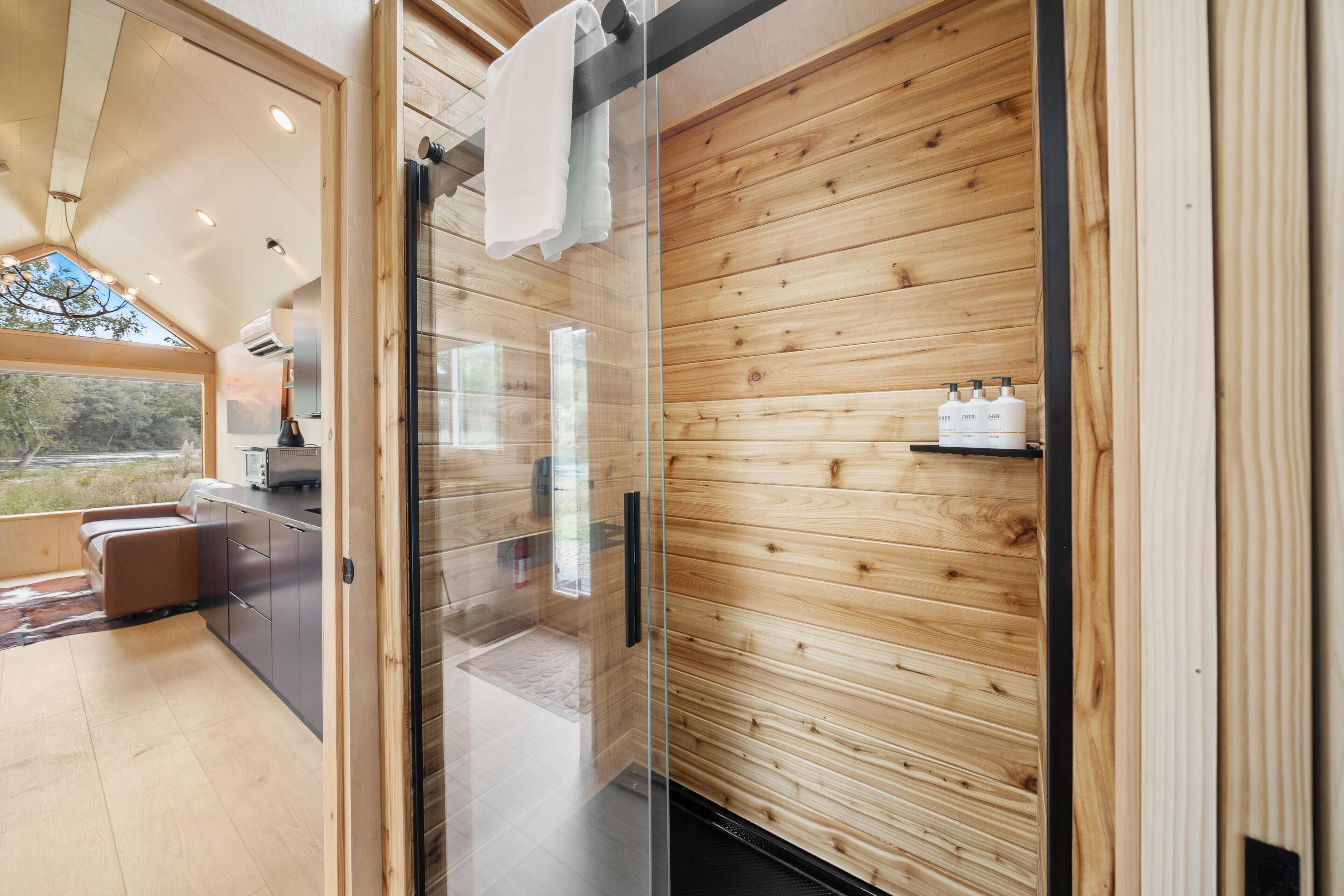 A modern interior with wooden panel walls, a glass door leading to a bathroom, and a kitchenette area.