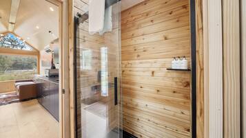 A modern interior with wooden panel walls, a glass door leading to a bathroom, and a kitchenette area.