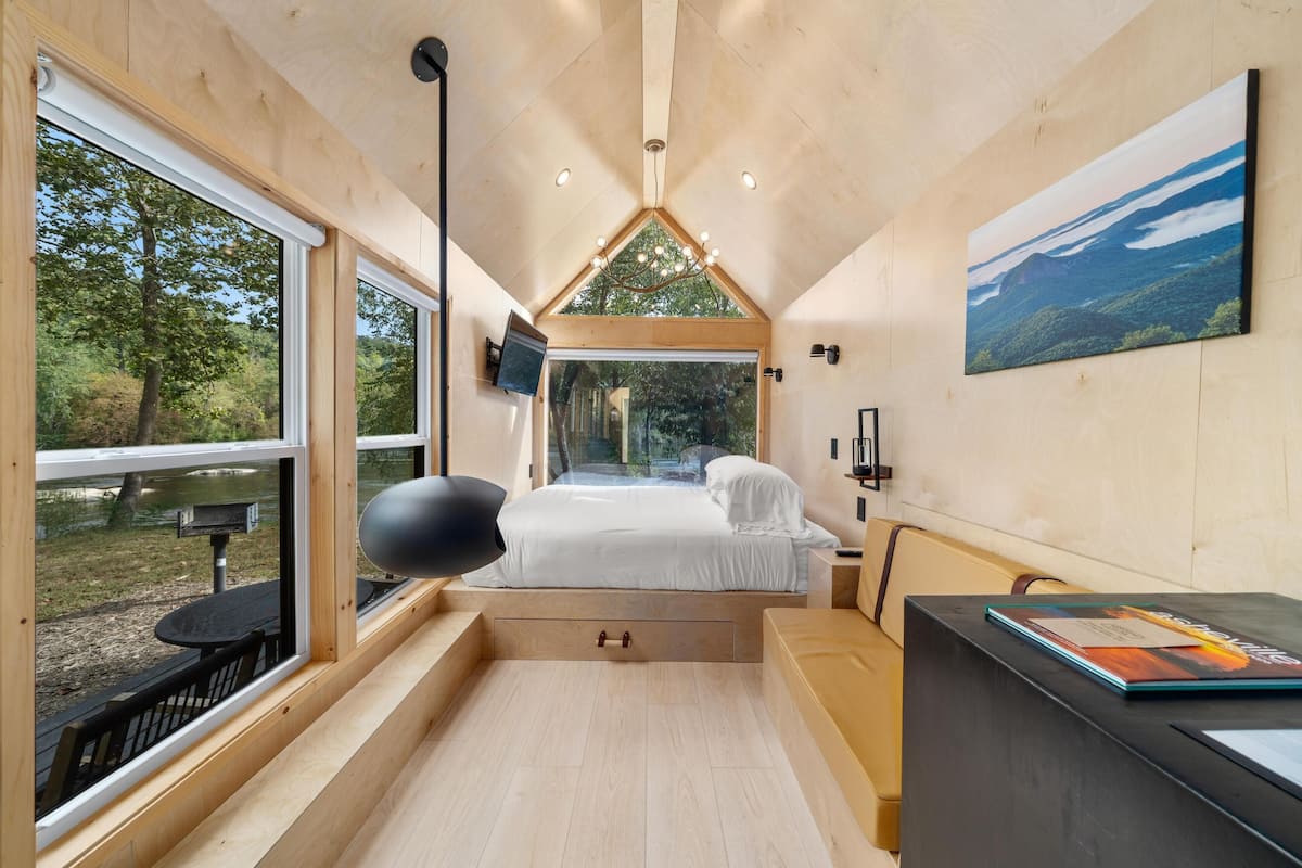 Une chambre moderne et compacte, dotée d’un lit, d’un bureau et d’une grande fenêtre donnant sur l’extérieur.