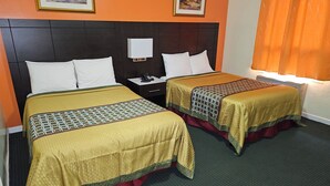 A hotel room with two beds, each with a patterned bedspread and pillows. There is a nightstand with a phone and a wall-mounted light. - Norvic Motel (Sudbury)