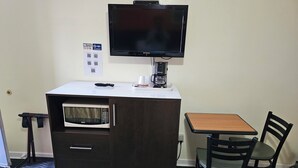 A compact room with a kitchenette, a flat-screen TV, a coffee maker, a microwave, a small table, and a chair. - Norvic Motel (Sudbury)