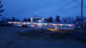 A two-story building with a covered front porch, a driveway with parked cars, and a stone pathway leading to the entrance. - Norvic Motel (Sudbury)