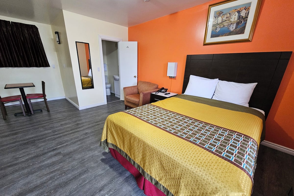 Quarto de hotel com cama, cadeira, mesa e banheiro visível por uma porta aberta.
